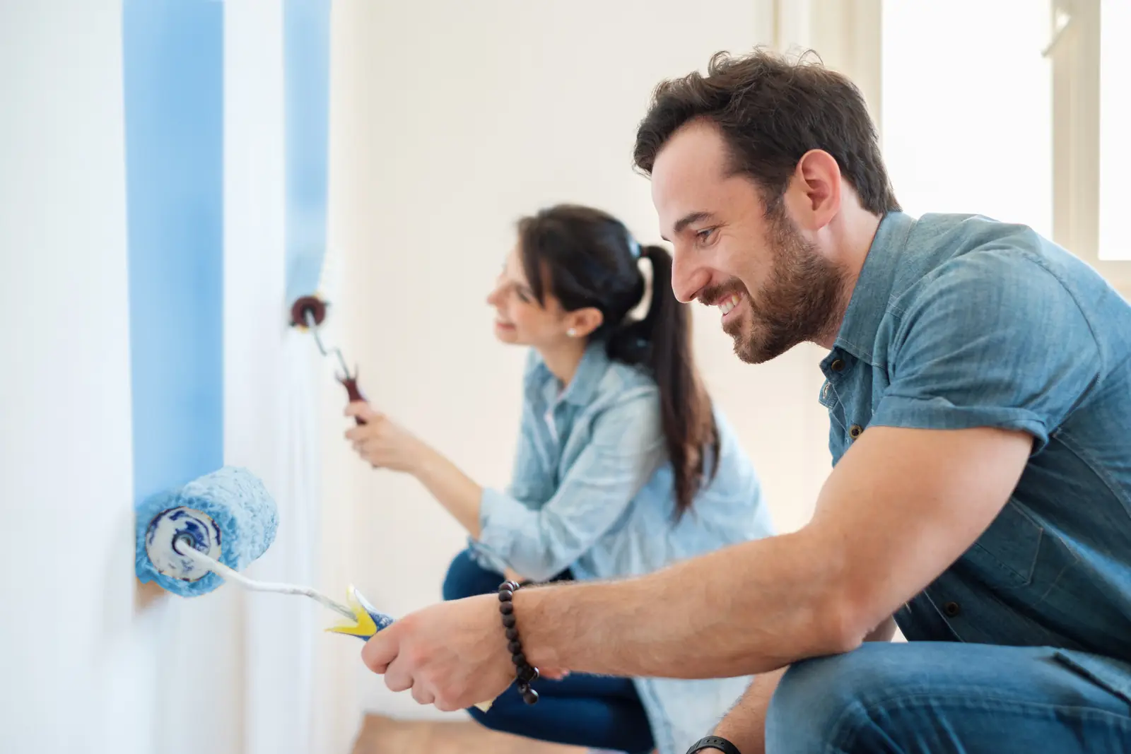 Pareja pintando una pared de azul claro en su casa